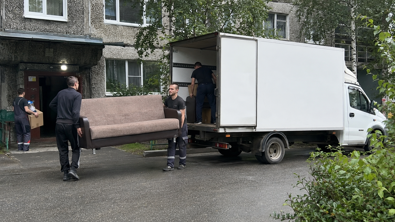 Грузчики несут мебель во дворе дома